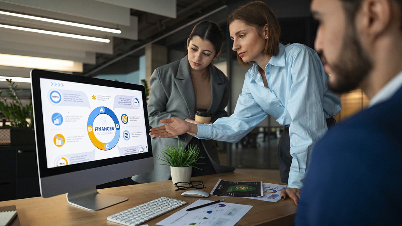 Verslo komanda analizuoja finansinę infografiką kompiuterio ekrane biuro aplinkoje