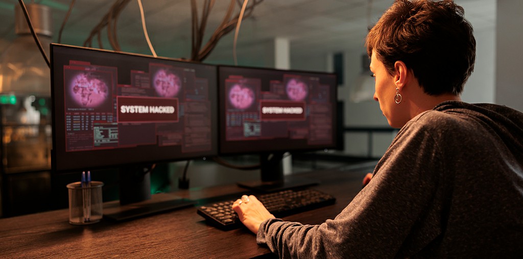 Asmuo prie kompiuterio su įsilaužimo pranešimu ekrane – sistema nulaužta